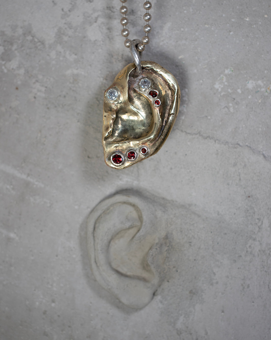 Ear pendant. Brass, 5 garnet stones, 2 zircons. / Wisior w kształcie ucha. Mosiadz, 5 kamieni granatów, 2 cyrkonie.