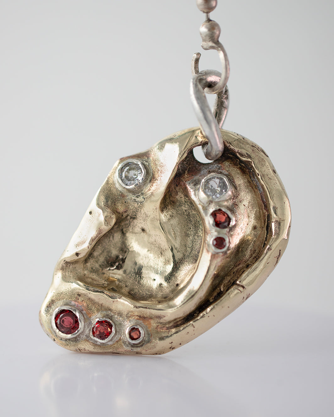Ear pendant. Brass, 5 garnet stones, 2 zircons. / Wisior w kształcie ucha. Mosiadz, 5 kamieni granatów, 2 cyrkonie.