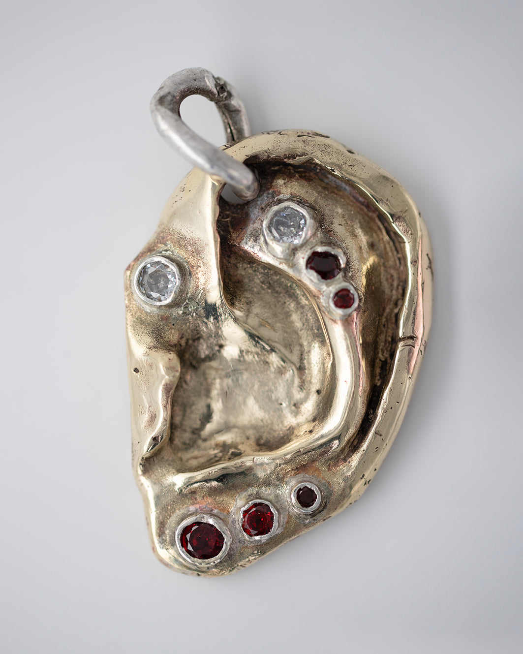Ear pendant. Brass, 5 garnet stones, 2 zircons. / Wisior w kształcie ucha. Mosiadz, 5 kamieni granatów, 2 cyrkonie.